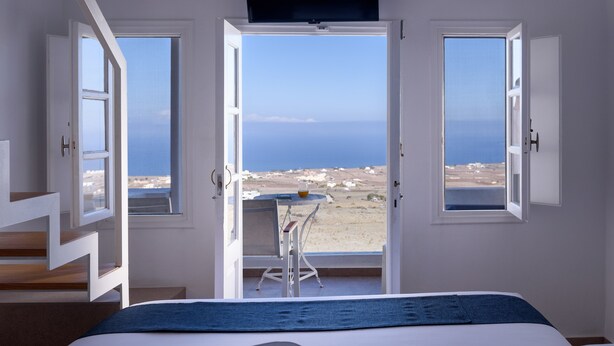 A bedroom with a bed, a desk, and a view of the sea. - Muses Cycladic Suites (Santorini)