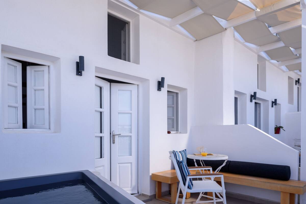 Un espace de vie extérieur moderne comprenant une piscine, un coin salon avec une table et des chaises, ainsi qu’un escalier menant à un niveau supérieur.