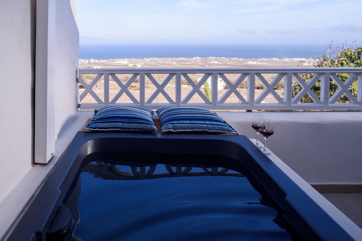 Une pièce baignée de lumière avec vue sur la mer, une balustrade blanche et une baignoire agrémentée de coussins bleus.