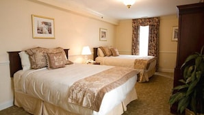 A hotel room with two beds, a nightstand, a lamp, a framed picture on the wall, and a large window with curtains. - Hotel Alcott (Cape May)