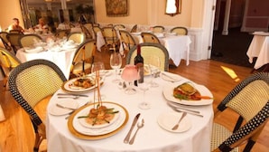 A dining area with round tables, chairs, and a bottle of wine. - Hotel Alcott (Cape May)