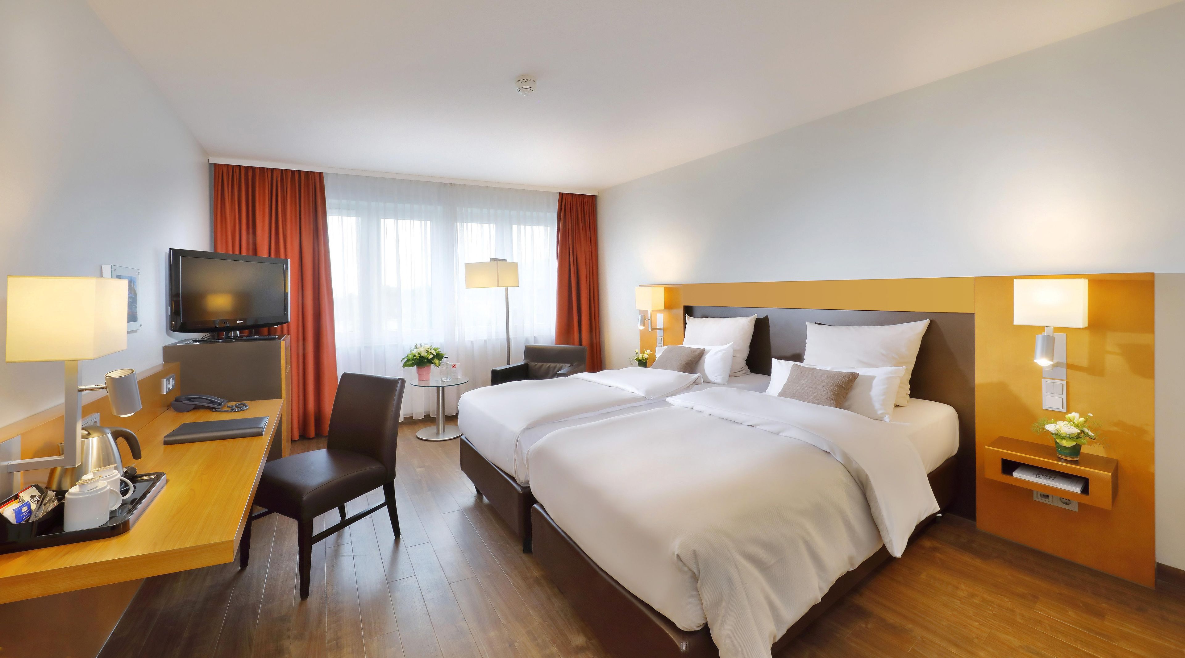 Habitación de hotel con cama, escritorio, silla, televisor y una mesita con una planta.