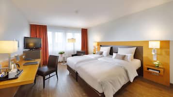 Habitación de hotel con cama, escritorio, silla, televisor y una mesita con una planta.
