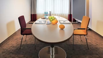 A hotel meeting room with a round table, two chairs, a fruit bowl, and a water dispenser.