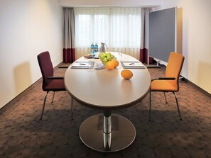 Een hotelvergaderruimte met een ronde tafel, twee stoelen, een schaal fruit en een waterdispenser.