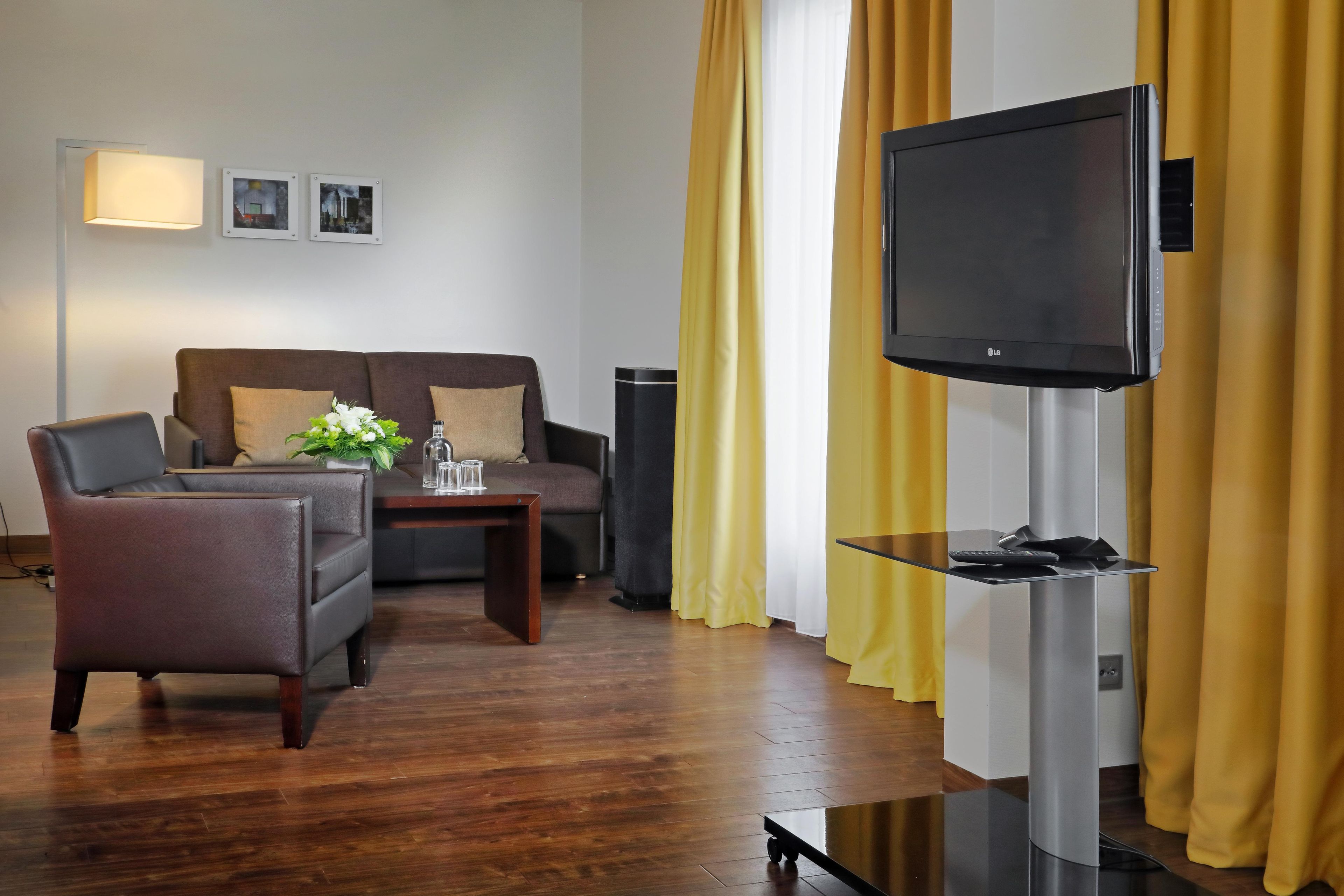A modern living room with a sofa, armchair, coffee table, and a flat-screen TV mounted on a stand.