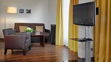 A modern living room with a sofa, armchair, coffee table, and a flat-screen TV mounted on a stand.