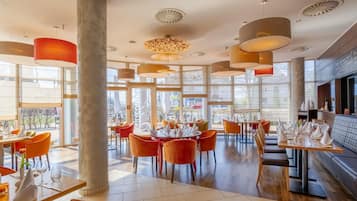 A modern restaurant interior with high ceilings, large windows, and a variety of seating arrangements.