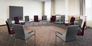 Ein Konferenzraum mit einer Sitzordnung in Kreisförmigkeit, einer Whiteboard und einem Getränkekühler.