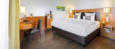 A hotel room with a bed, desk, chair, and a small table with a phone and a vase of flowers.