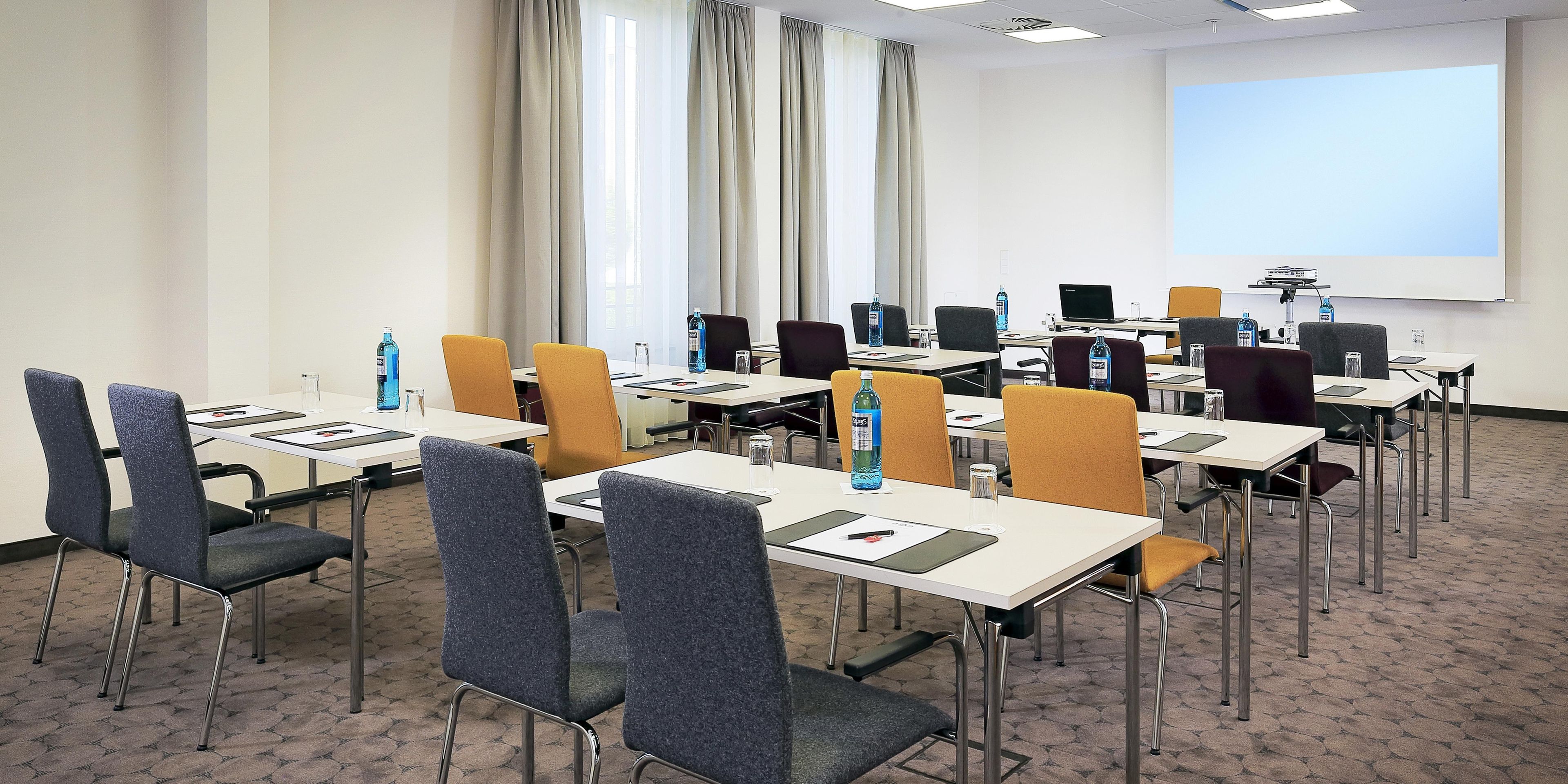 Une salle de conférence équipée de plusieurs tables, de chaises et d’un écran de projection.