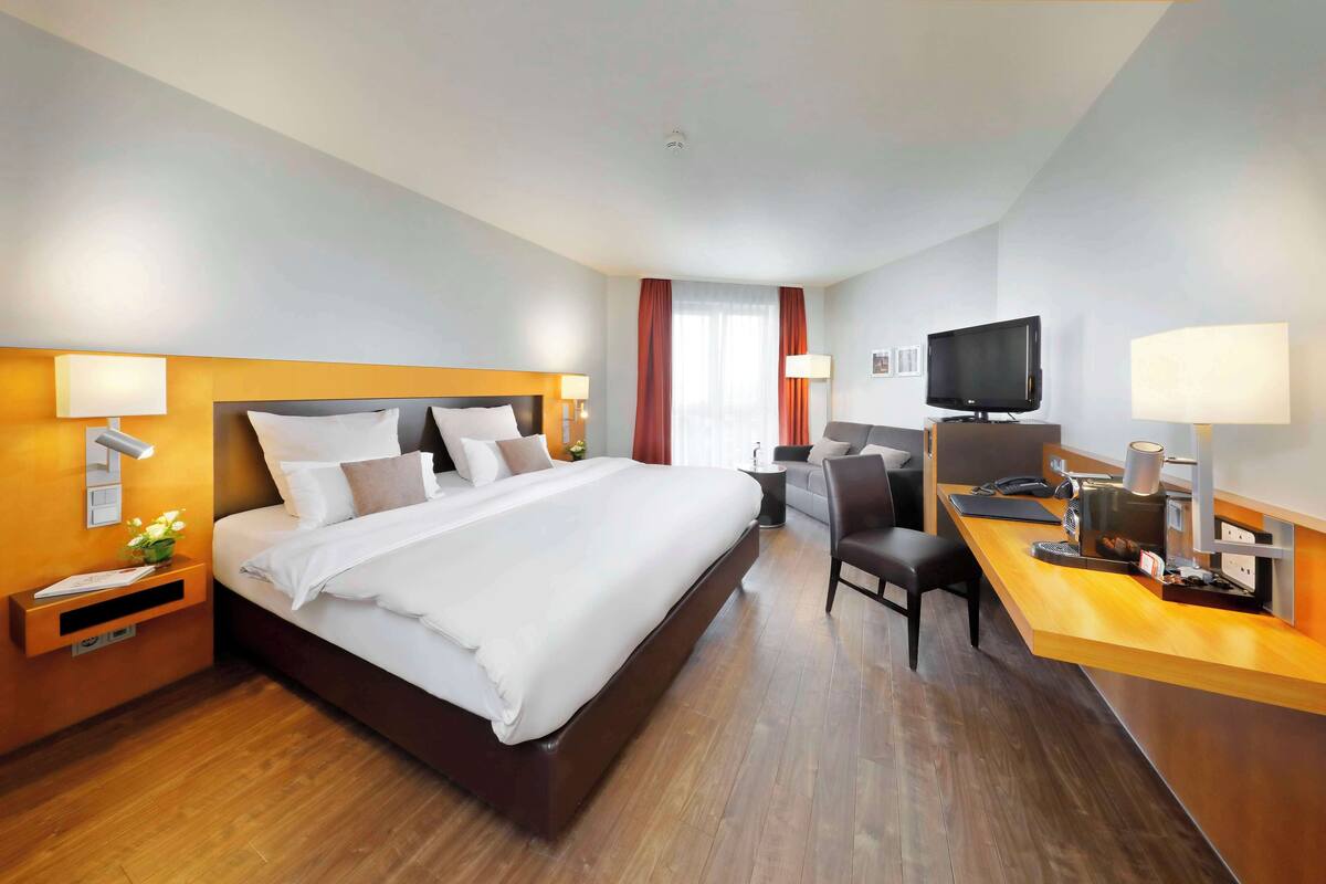 Une chambre d’hôtel avec un grand lit, un bureau avec un ordinateur, une télévision et une chaise.