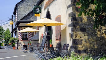 Outdoor seating with umbrellas, a stone building, and a sign indicating a restaurant.