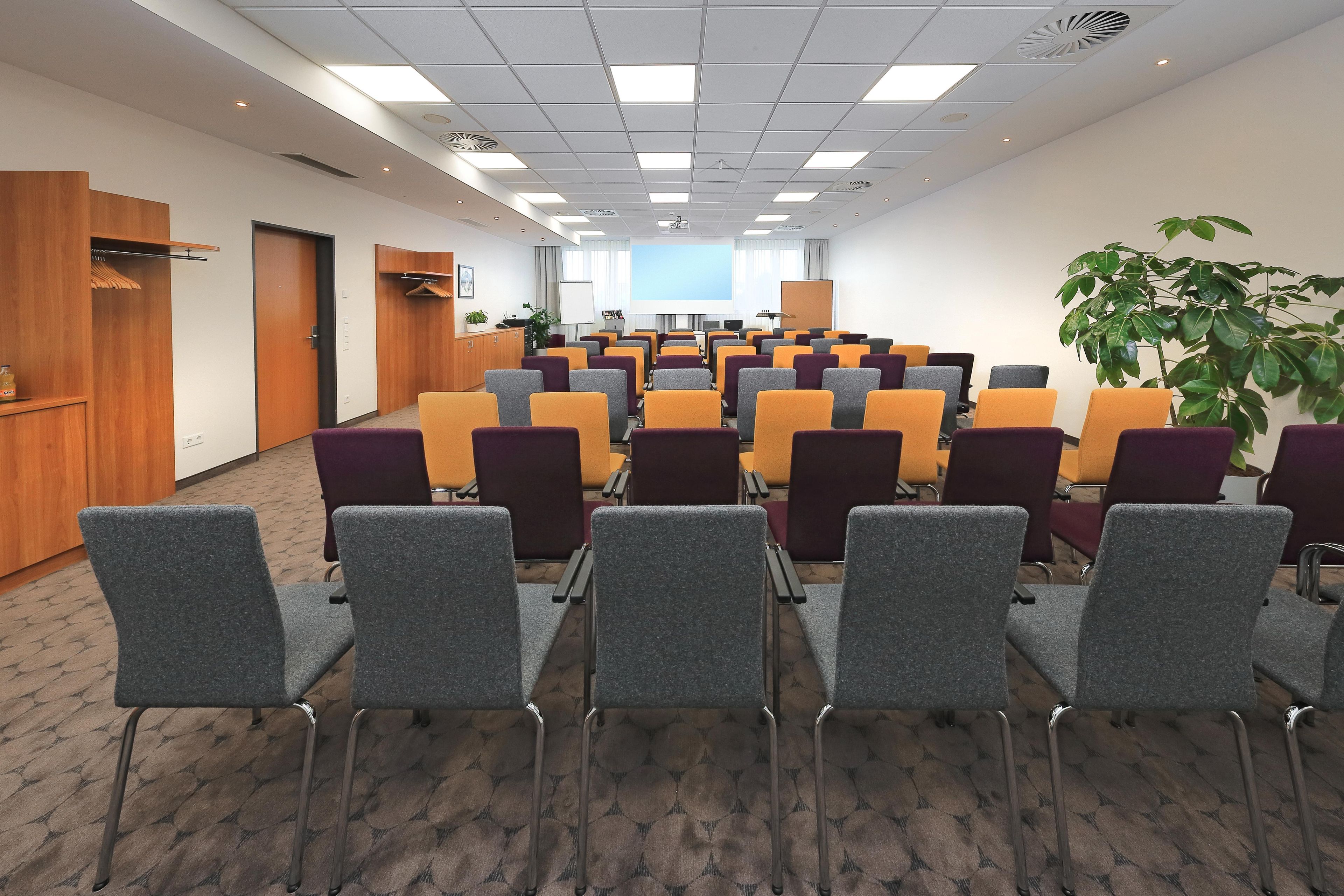 Ein Konferenzraum mit Reihen von Stühlen, einer Projektionsleinwand und einer Whiteboard.