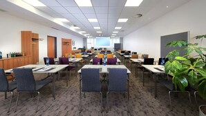 A conference room with multiple tables and chairs, a large screen at the front, and a plant in the corner. - Best Western Premier IB Hotel Friedberger Warte (Frankfurt)