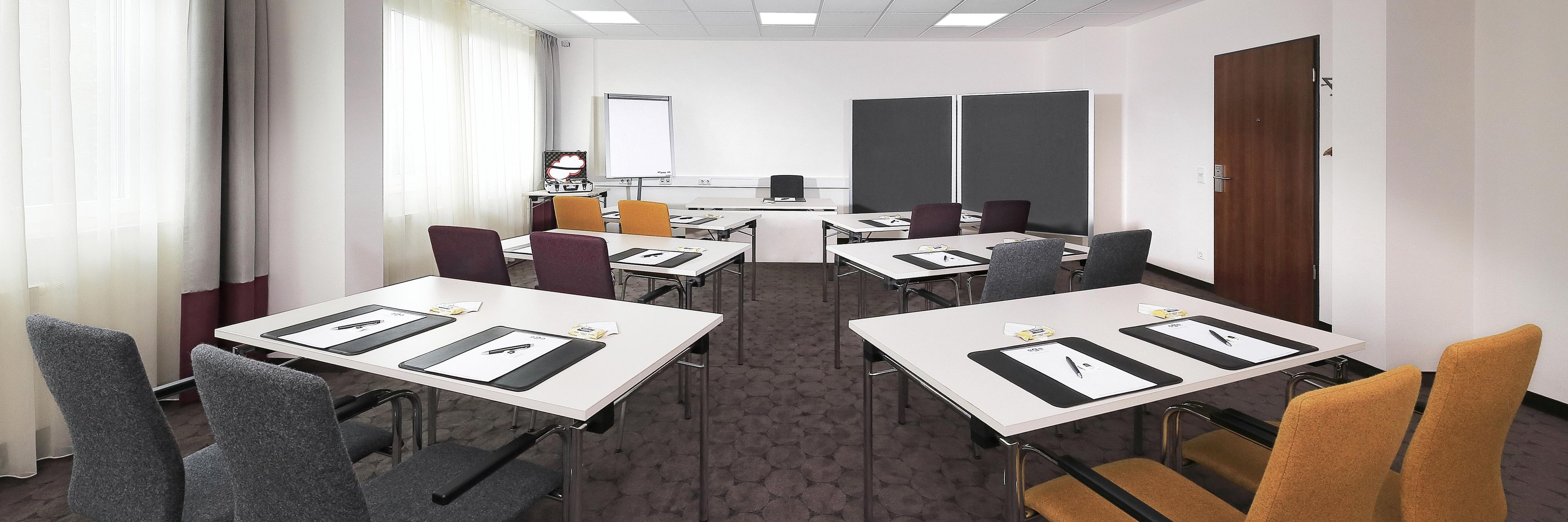 A conference room with tables, chairs, a whiteboard, and a projector screen.