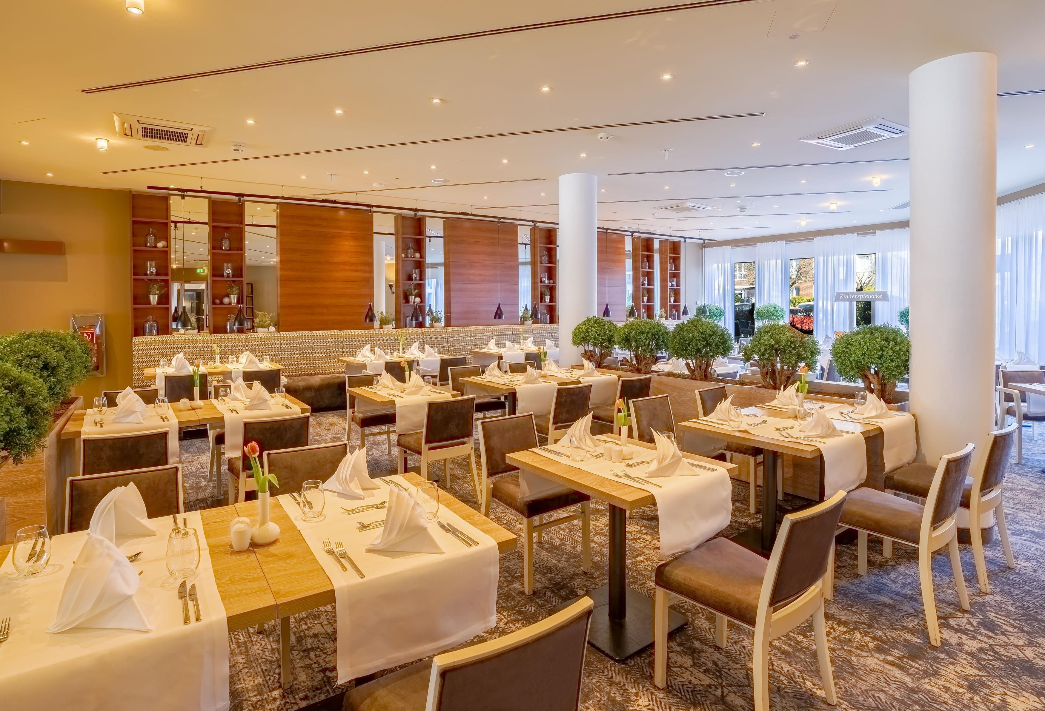 Une salle à manger d’hôtel avec de nombreuses tables dressées pour accueillir les clients, présentant un design intérieur moderne agrémenté d’éléments en bois et dotée d’un sol recouvert de moquette.