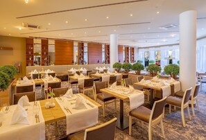 A hotel dining area with multiple tables set for guests, featuring a modern interior design with wooden accents and a carpeted floor. - Best Western Premier IB Hotel Friedberger Warte (Frankfurt)