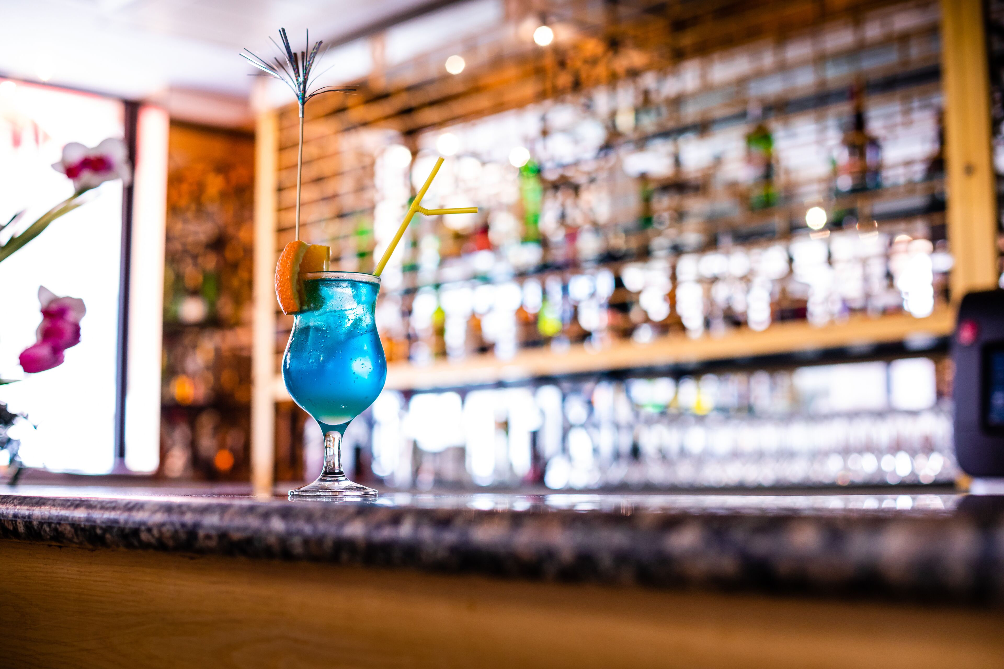 A bar setting with a blue cocktail, a straw, and a garnish.