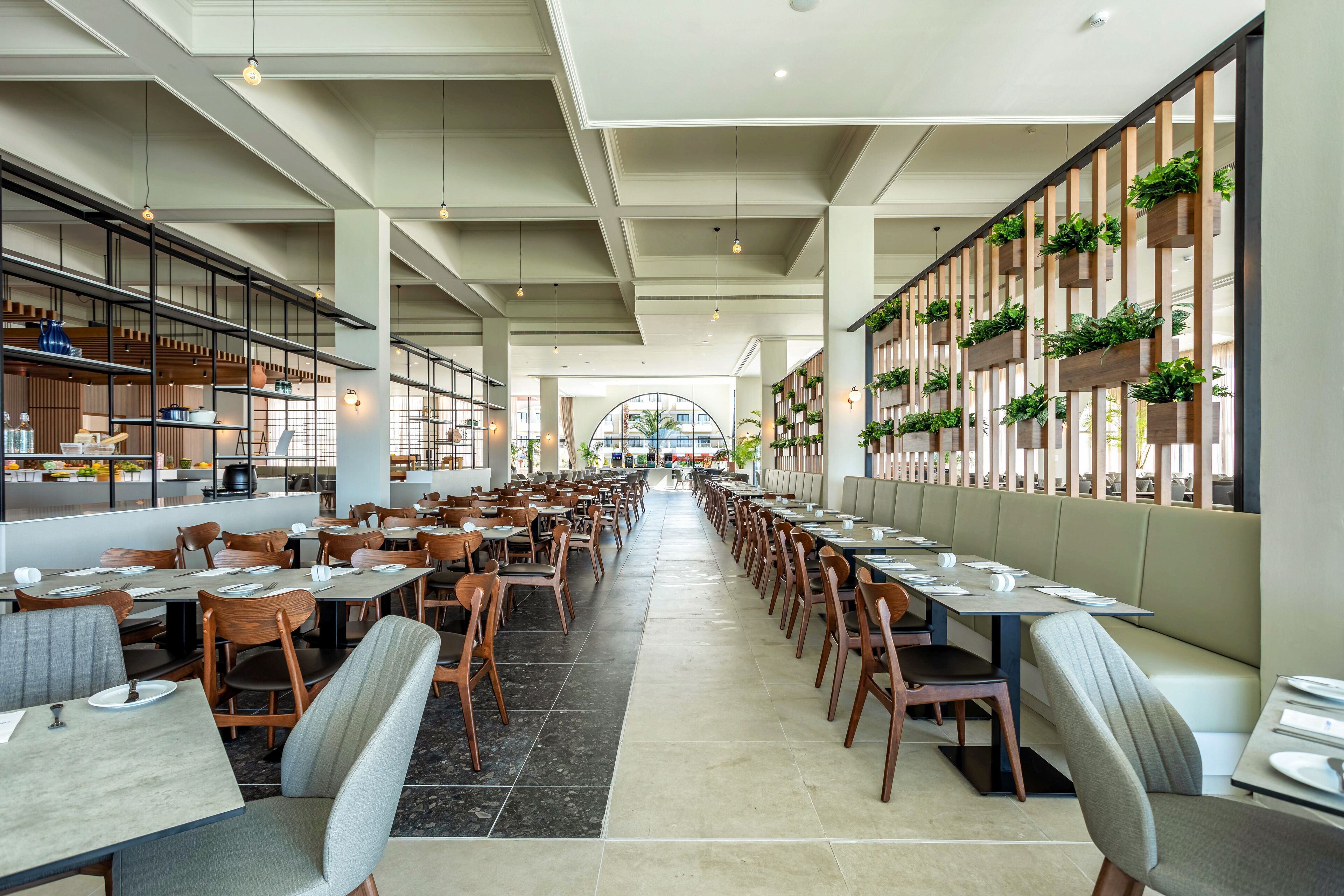 A spacious restaurant with high ceilings, wooden beams, and a central aisle. Tables are arranged on both sides, with some seating along the walls.