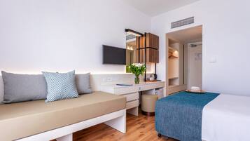 A modern hotel room with a sofa, a bed, a desk with a mirror, a television, and a small bathroom.