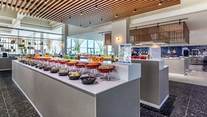 Un moderno vestíbulo de hotel con una zona de buffet central que ofrece diversas opciones de comida.