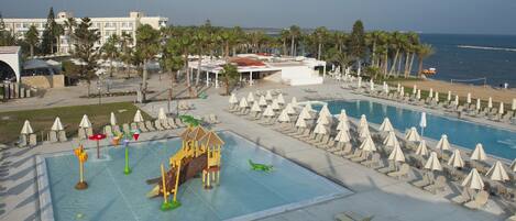 Zona de piscina en un resort, con varias piscinas, sillas de descanso, sombrillas y palmeras.