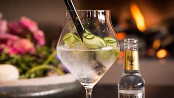 Ett glas med is och gurkskivor, en flaska Fever-Tree-tonik och en suddig bakgrund med blommor.