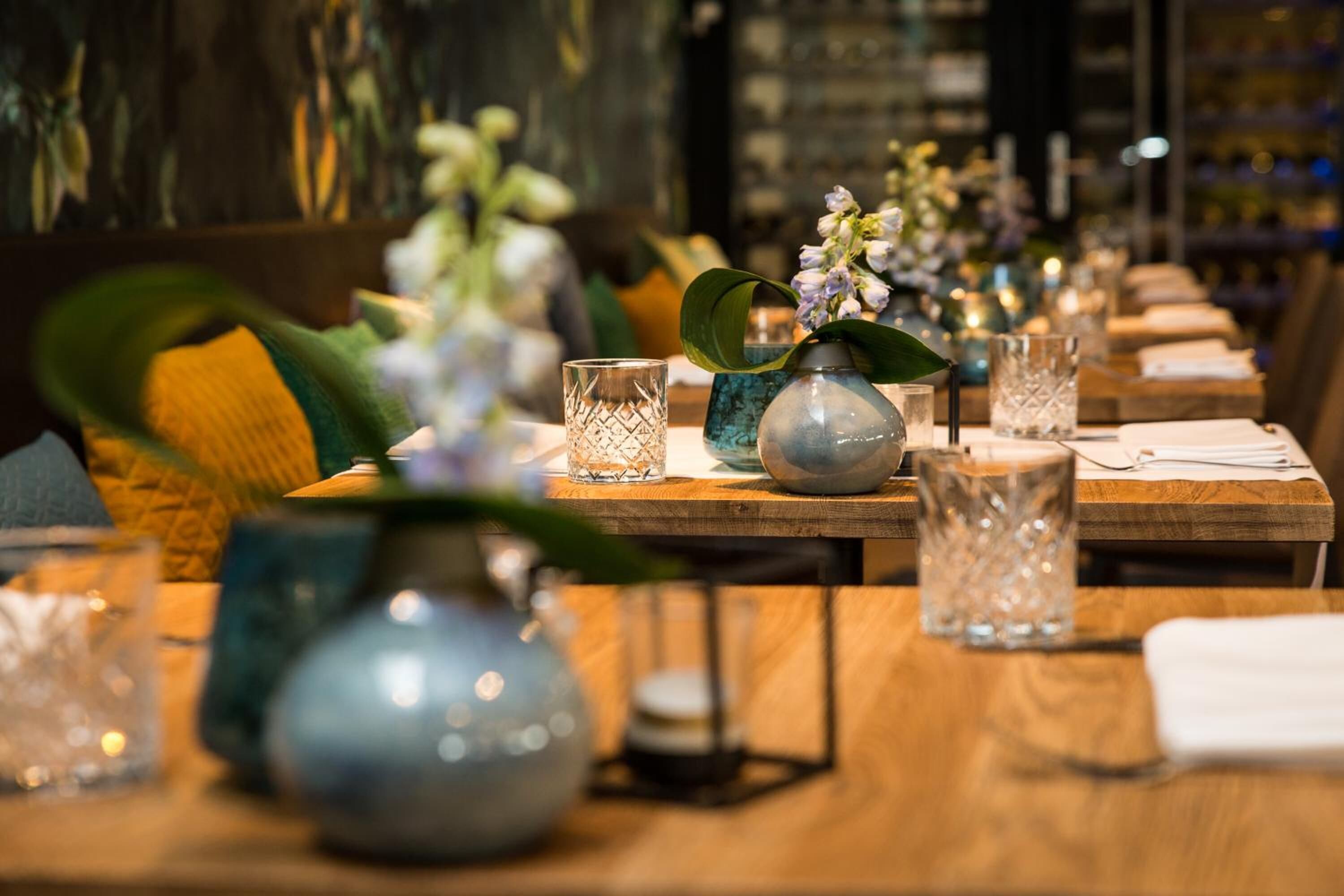 A restaurant setting with wooden tables, glassware, and floral centerpieces.
