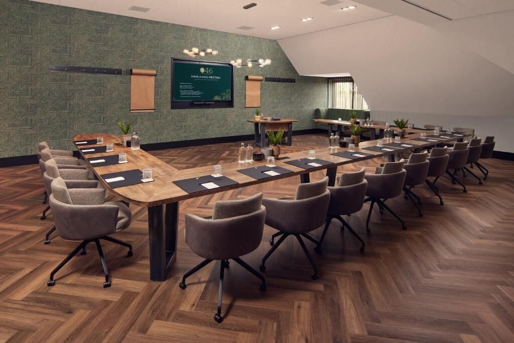 A conference room with a long table, multiple chairs, a screen, and a green textured wall.