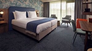 A hotel room with a large bed, a desk, a chair, and a window with curtains. - Van Der Valk Hotel Stein - Urmond (Urmond)