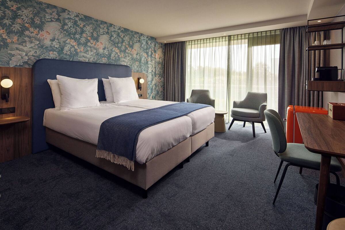 A hotel room with a large bed, a desk, a chair, and a window with curtains.