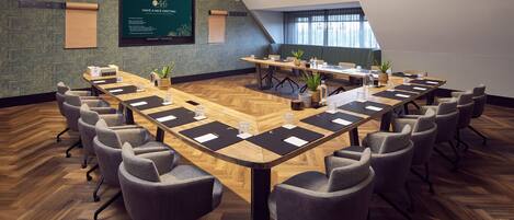 A conference room with a long table, multiple chairs, and a green wall with a framed poster.