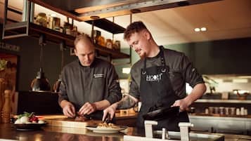 Twee koks in een keuken met roestvrijstalen apparatuur en houten planken.