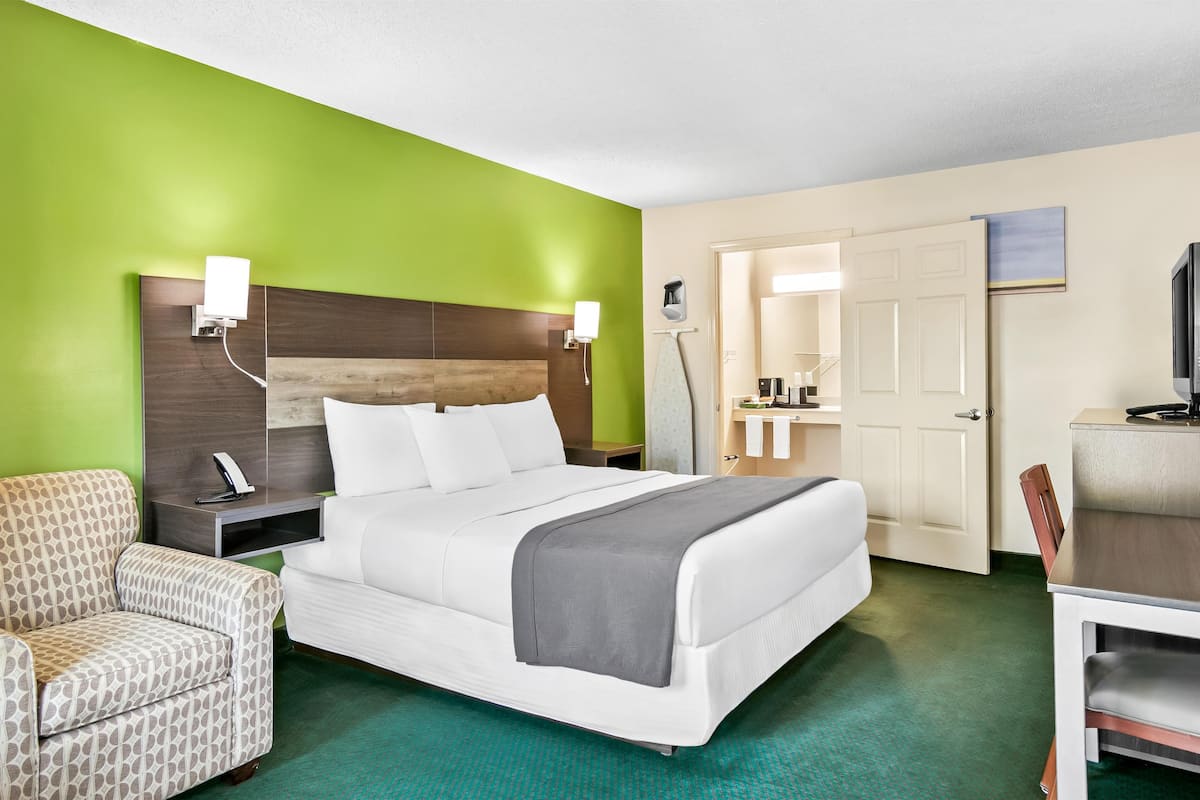 Ein Hotelzimmer mit Bett, Sessel, Schreibtisch, Fernseher und einem durchgegangenen Tür erkennbaren Badezimmer.