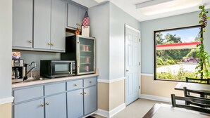 A compact kitchen with grey cabinets, a microwave, and a small refrigerator. There's a window with a view of a parking lot and greenery. - Americas Best Value Inn Rome (Rome)