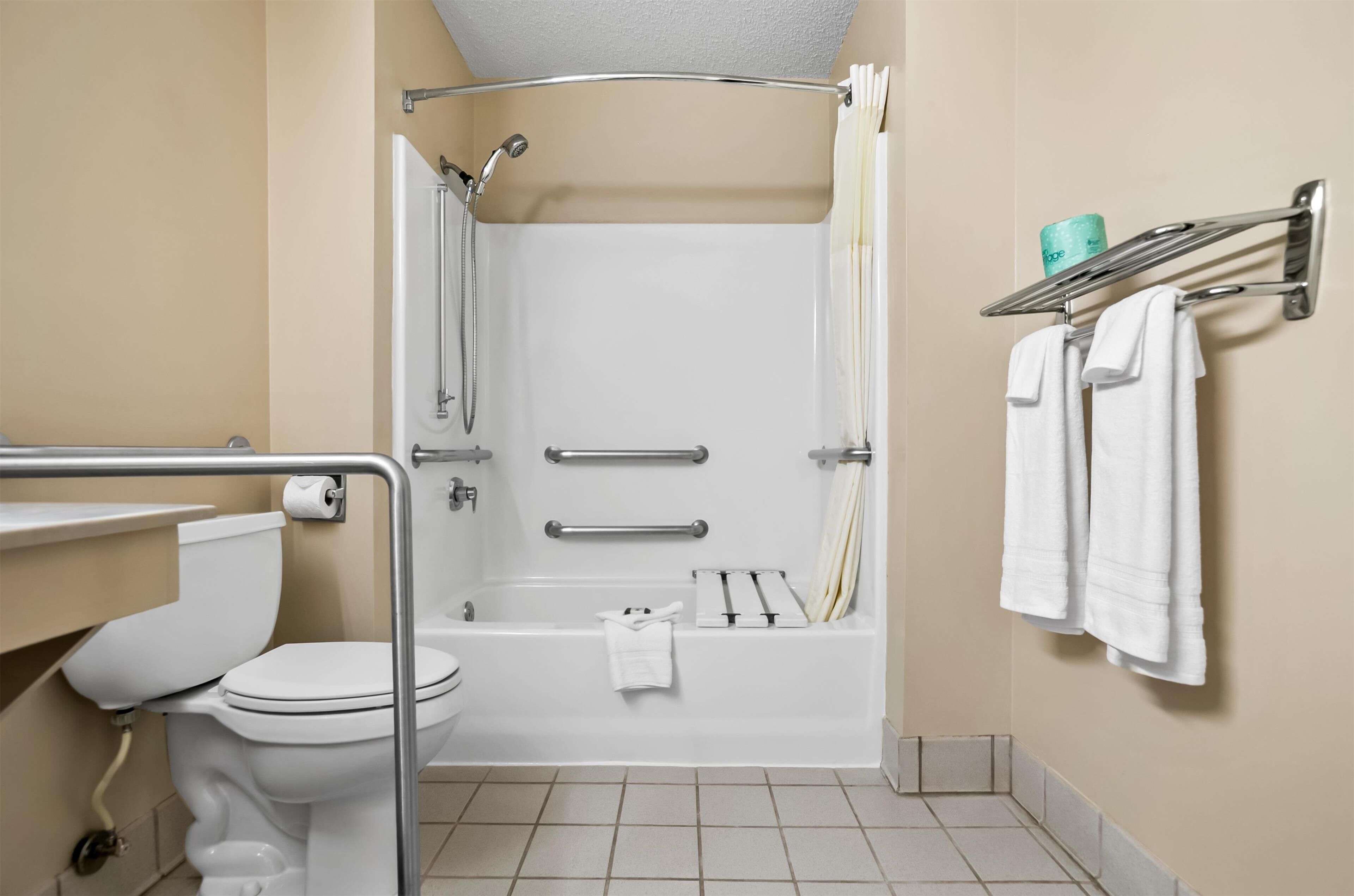 Un baño con inodoro, ducha con puerta de cristal, toallero con toallas y dispensador de papel higiénico.
