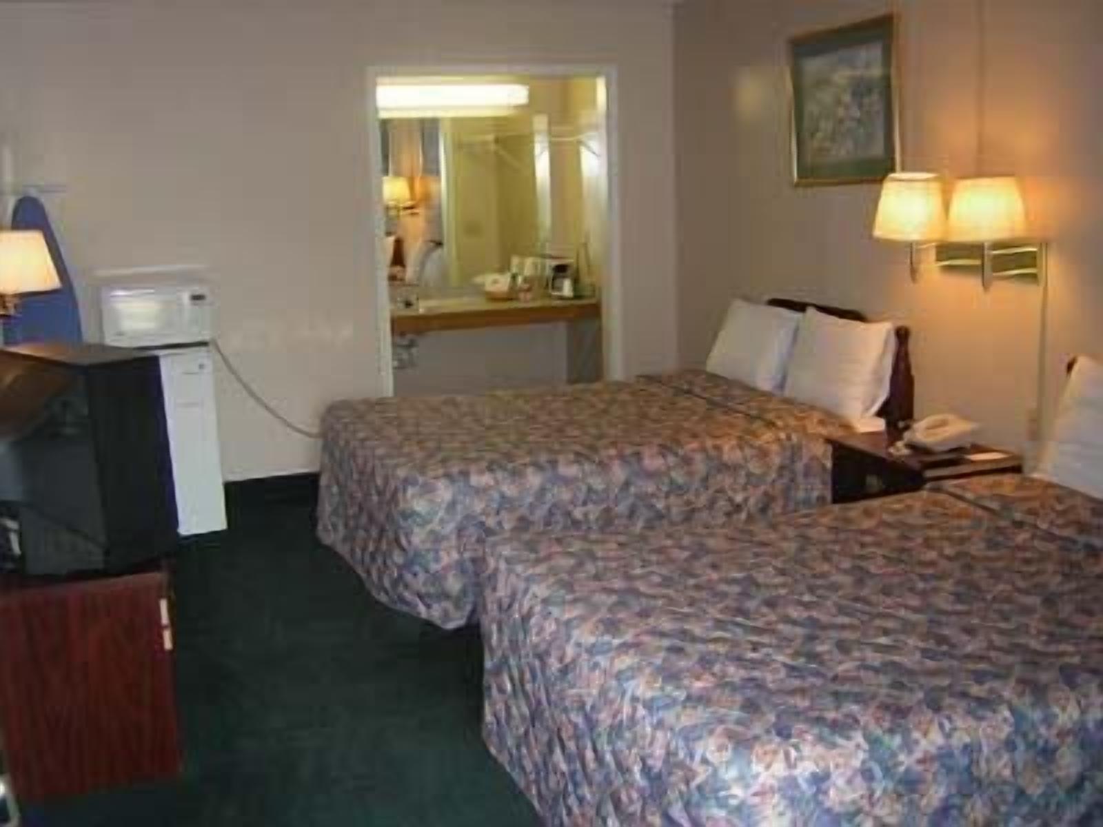 Una habitación de hotel con dos camas, un escritorio con computadora, una lámpara y un microondas.