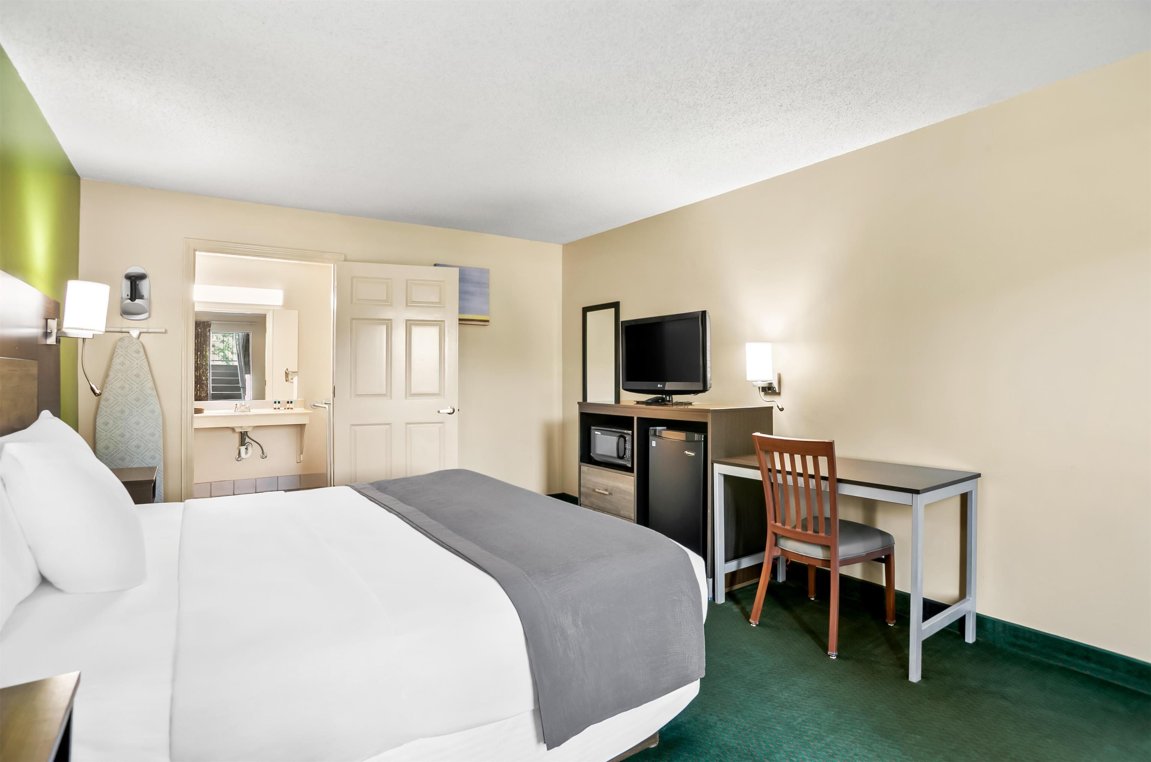 A hotel room with a bed, desk, chair, television, and a small kitchenette.