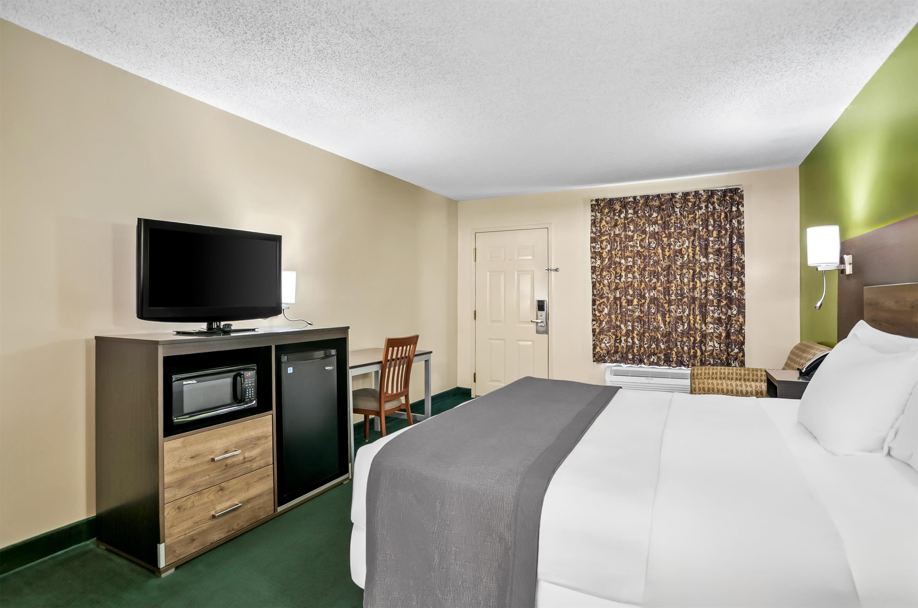 A hotel room with a bed, a TV, a microwave, a desk, and a chair.