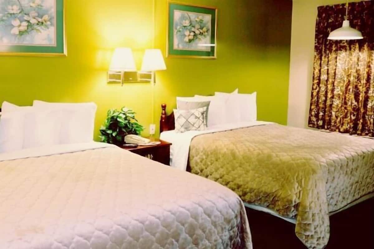 Ein Hotelzimmer mit zwei Betten, einem Nachttisch, einer Lampe und zwei gerahmten floralen Bildern an der Wand.