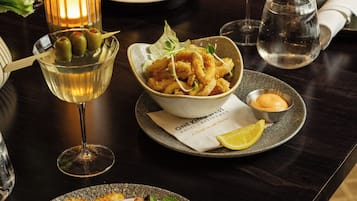 Una mesa de comedor con varios platos, entre ellos una ensalada, pan y mariscos, junto con copas de vino.