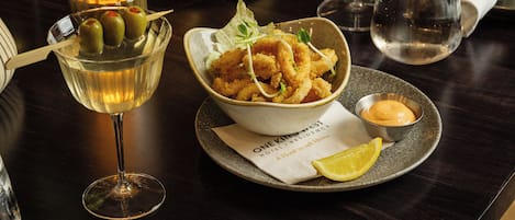 Una mesa de comedor con varios platos, entre ellos una ensalada, pan y mariscos, junto con copas de vino.