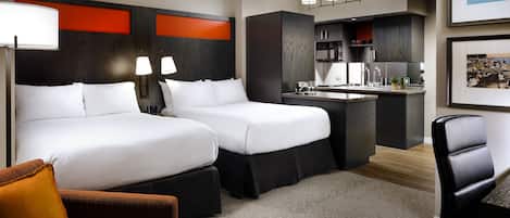Ein Hotelzimmer mit zwei Betten, einer Küchenzeile, einem Essbereich und einer Sitzecke mit Sessel und Hocker.