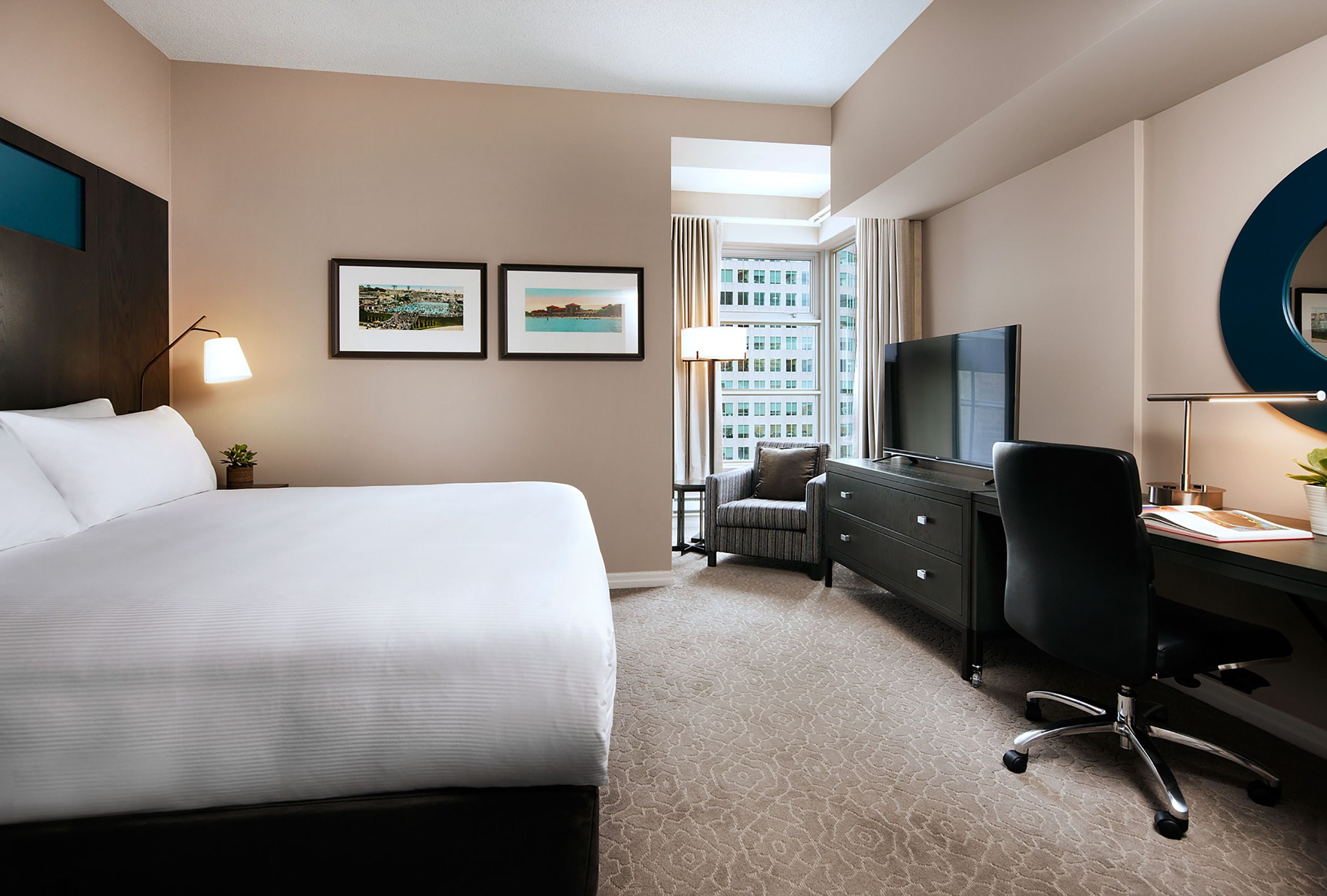 A hotel room with a large bed, a desk with a chair, a television, and framed pictures on the wall.