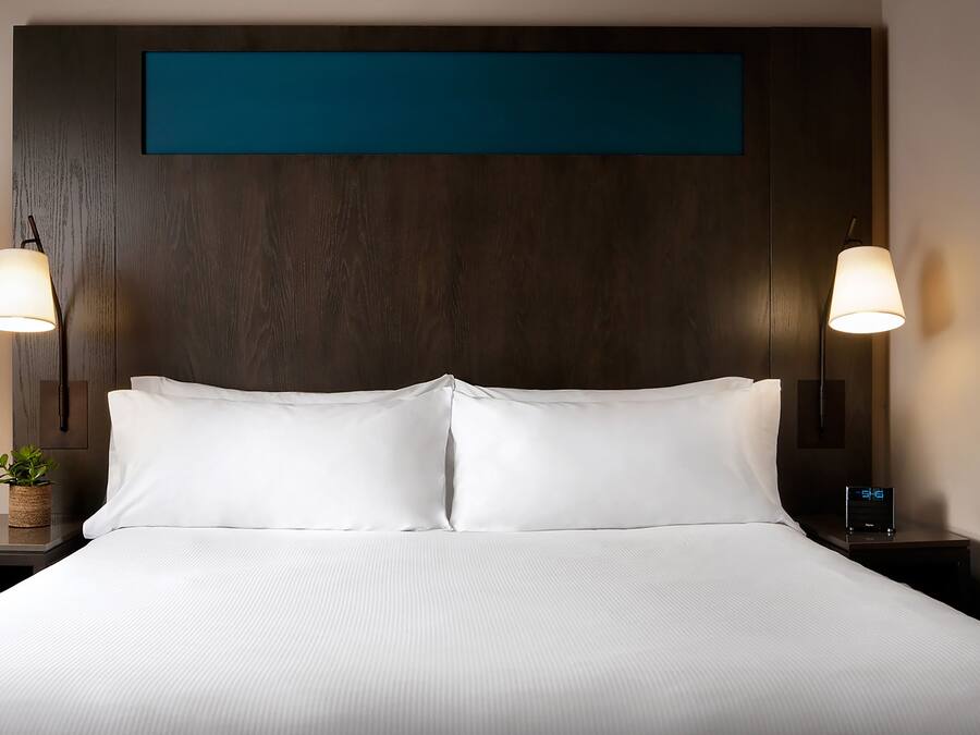 Una cama bien hecha con sábanas blancas, un cabecero de madera oscura y dos lámparas de noche.