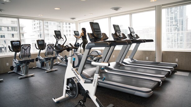 A gym with stationary bikes, treadmills, and a large window with a city view. - One King West Hotel & Residence (Toronto)
