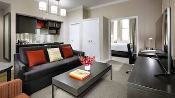 A modern hotel room with a living area, kitchenette, and a separate bedroom.