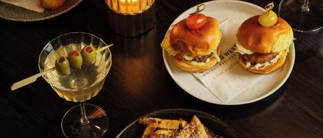 A dining table with various dishes, including burgers, fries, and a salad, along with wine glasses and a lit candle.