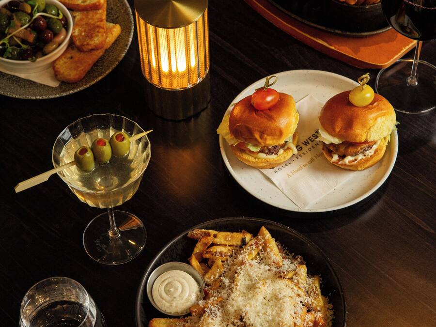 A dining table with various dishes, including burgers, fries, and a salad, along with wine glasses and a lit candle.